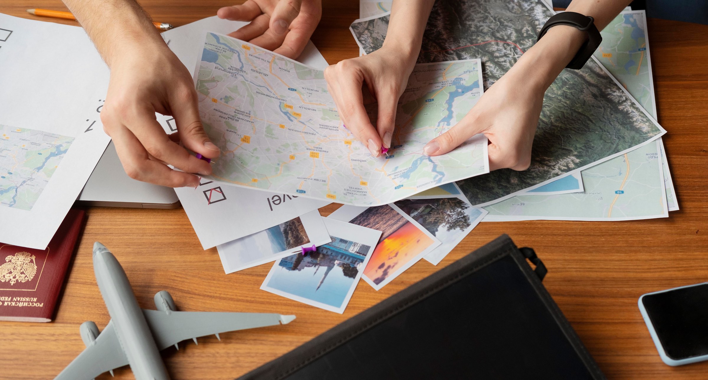 Travel planning desk with maps, documents, and hands placing pins on destinations